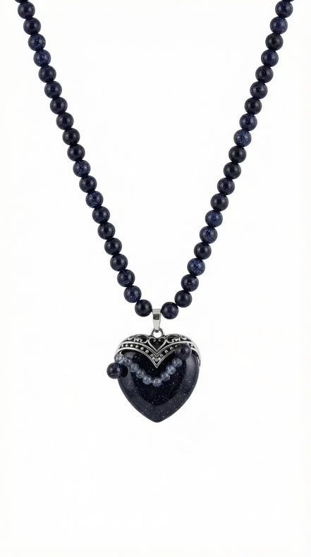 Colier pe fundal alb din mărgele albastre sclipitoare și pandantiv mare în formă de inimă cu montură argintie filigranată.
