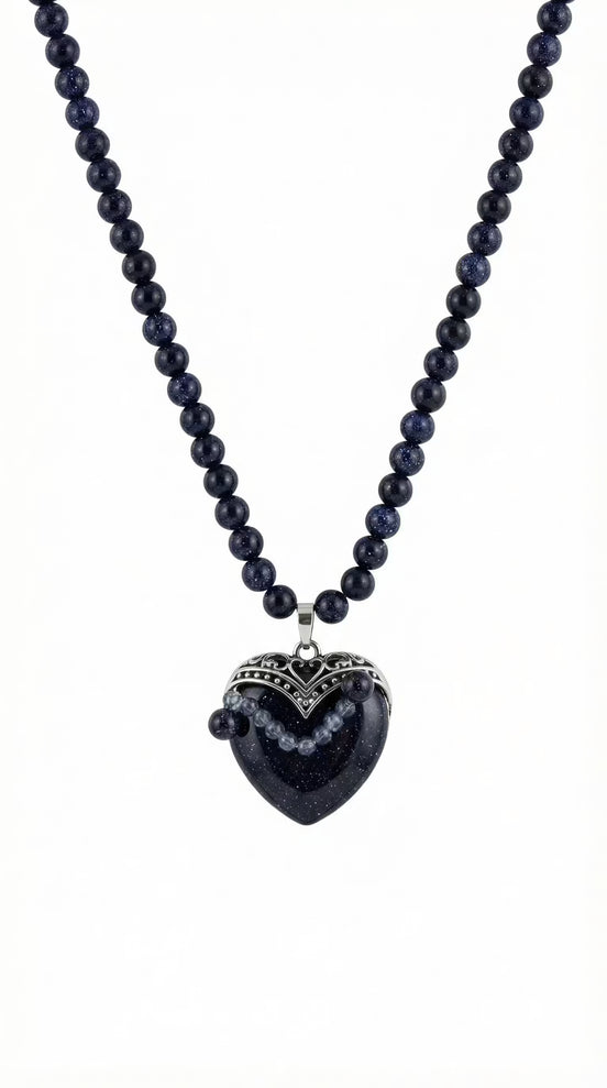 Colier pe fundal alb din mărgele albastre sclipitoare și pandantiv mare în formă de inimă cu montură argintie filigranată.