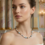 Femeie purtând un colier scurt la baza gâtului cu pietre bleu cubice și perle albe asortat la o rochie crem cu umerii goi.