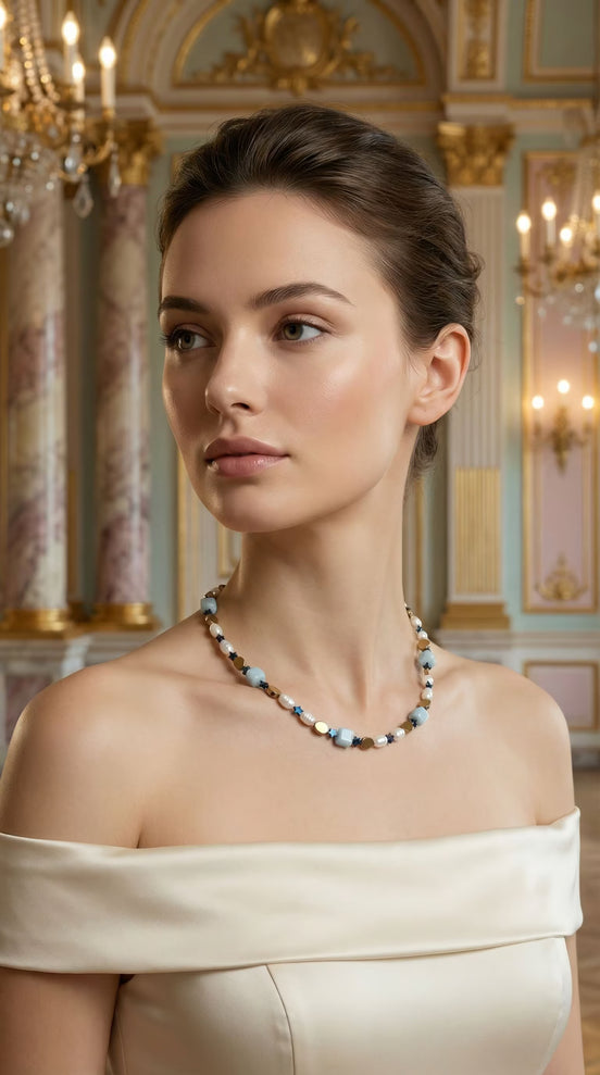 Femeie purtând un colier scurt la baza gâtului cu pietre bleu cubice și perle albe asortat la o rochie crem cu umerii goi.