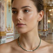 Femeie purtând un colier scurt la baza gâtului din pietre verzi fațetate și perlă alungită, asortat la o rochie crem cu umerii goi.