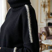 Prim-plan al umărului și gulerului unei malete negre evidențiind șiragul de perle albe și mărgele argintii aplicat pe cusătura raglan.