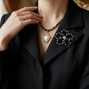 Prim-plan cu reverul satinat al unui sacou negru decorat cu o broșă în formă de floare din cristale negre și transparente.