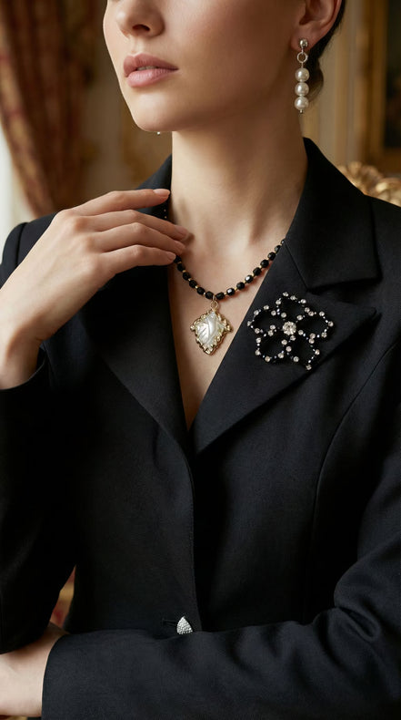Prim-plan cu reverul satinat al unui sacou negru decorat cu o broșă în formă de floare din cristale negre și transparente.