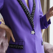 Vedere de aproape a buzunarului cu clapă neagră și cristale de pe un sacou mov și a nasturelui central strălucitor.