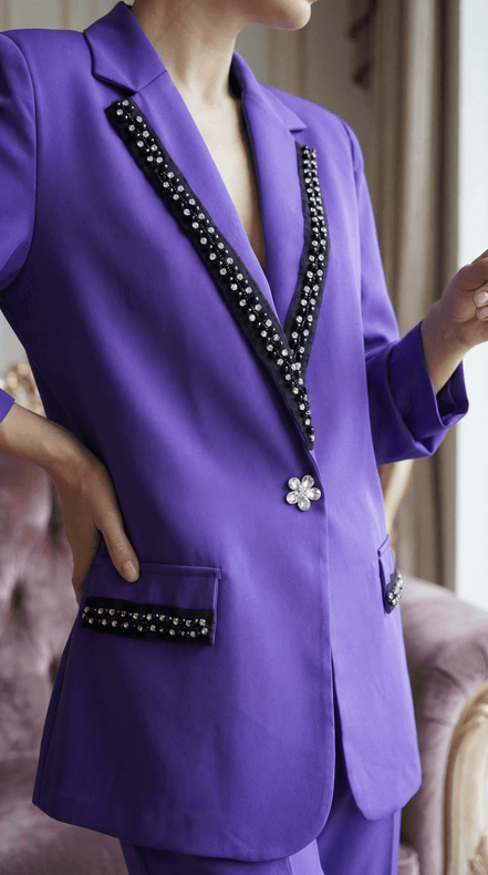 Vedere de aproape a buzunarului cu clapă neagră și cristale de pe un sacou mov și a nasturelui central strălucitor.