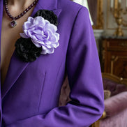 Prim-plan cu reverul unui sacou violet evidențiind aplicația manuală 3D compusă dintr-o floare satinată deschisă și elemente negre sclipitoare.