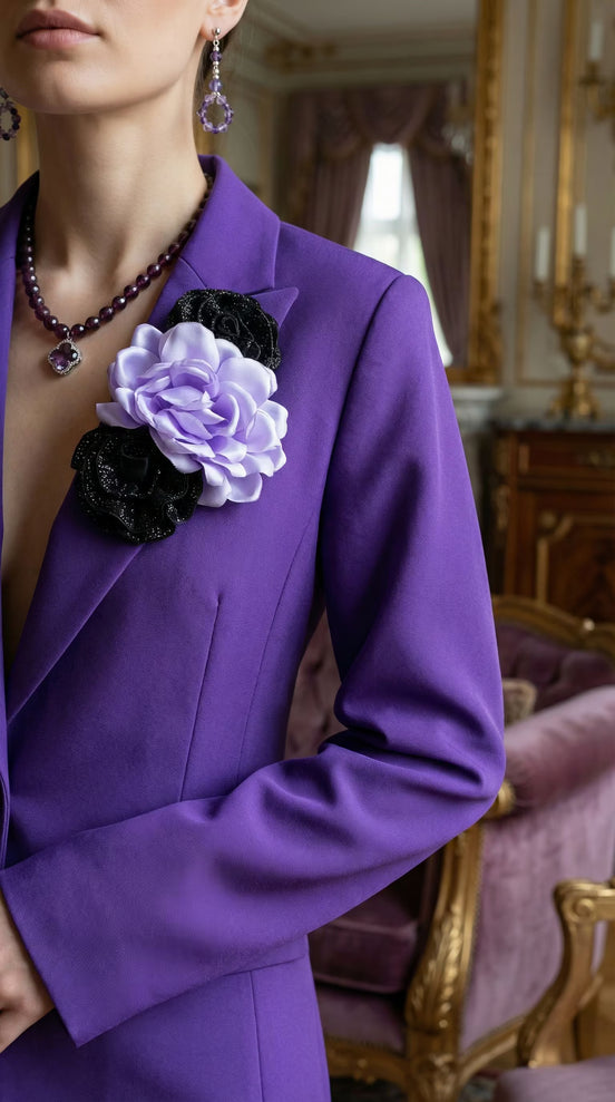 Prim-plan cu reverul unui sacou violet evidențiind aplicația manuală 3D compusă dintr-o floare satinată deschisă și elemente negre sclipitoare.