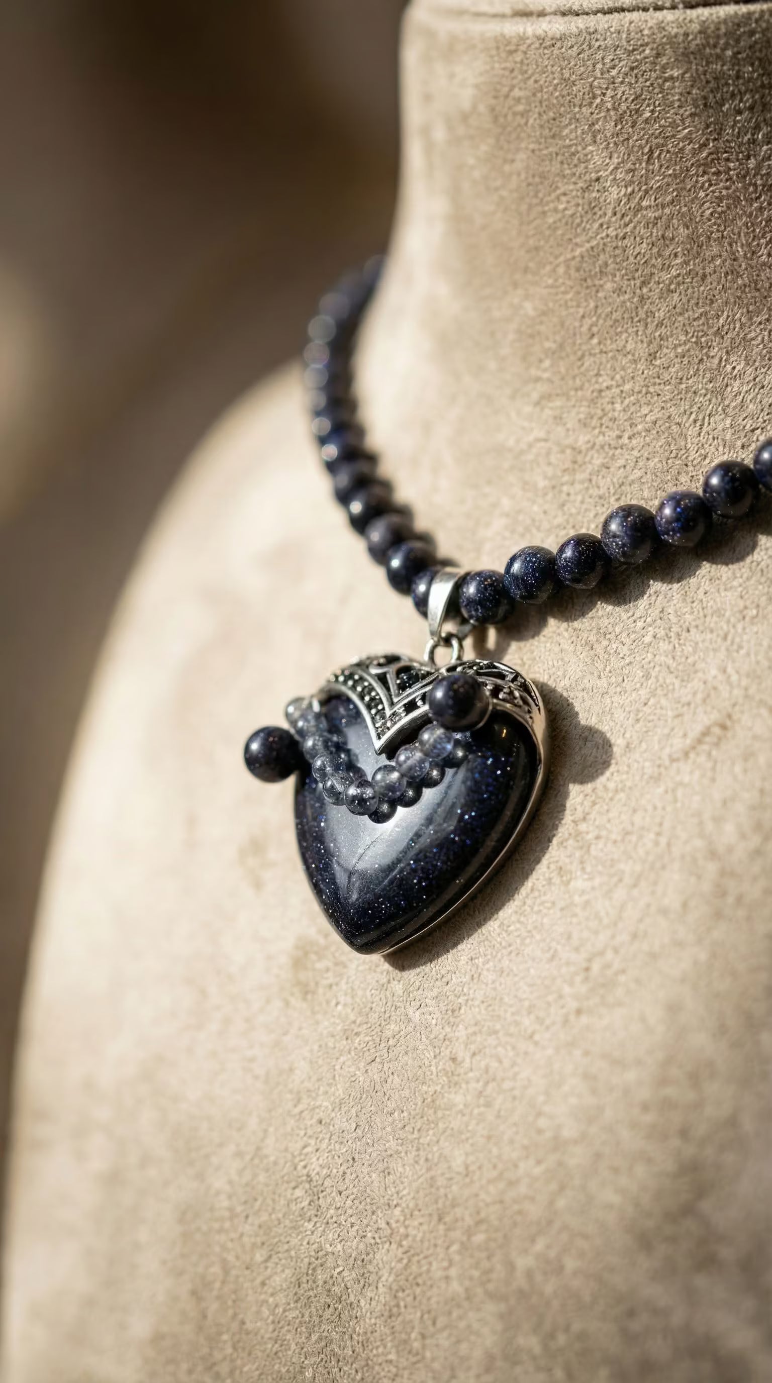 Prim-plan cu pandantivul inimă din piatra soarelui albastră evidențiind particule strălucitoare și detaliul decorativ din metal argintiu.