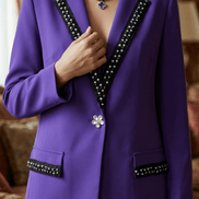 Prim-plan cu zona pieptului a sacoului mov arătând nasturele bijuterie în formă de floare și textura cristalelor aplicate pe rever.