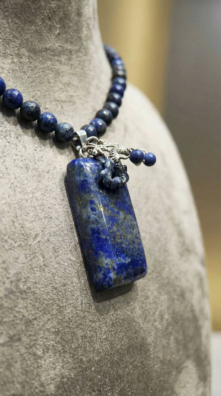 Prim-plan macro cu pandantivul dreptunghiular albastru cu incluziuni aurii și montură sub formă de dragon argintiu.