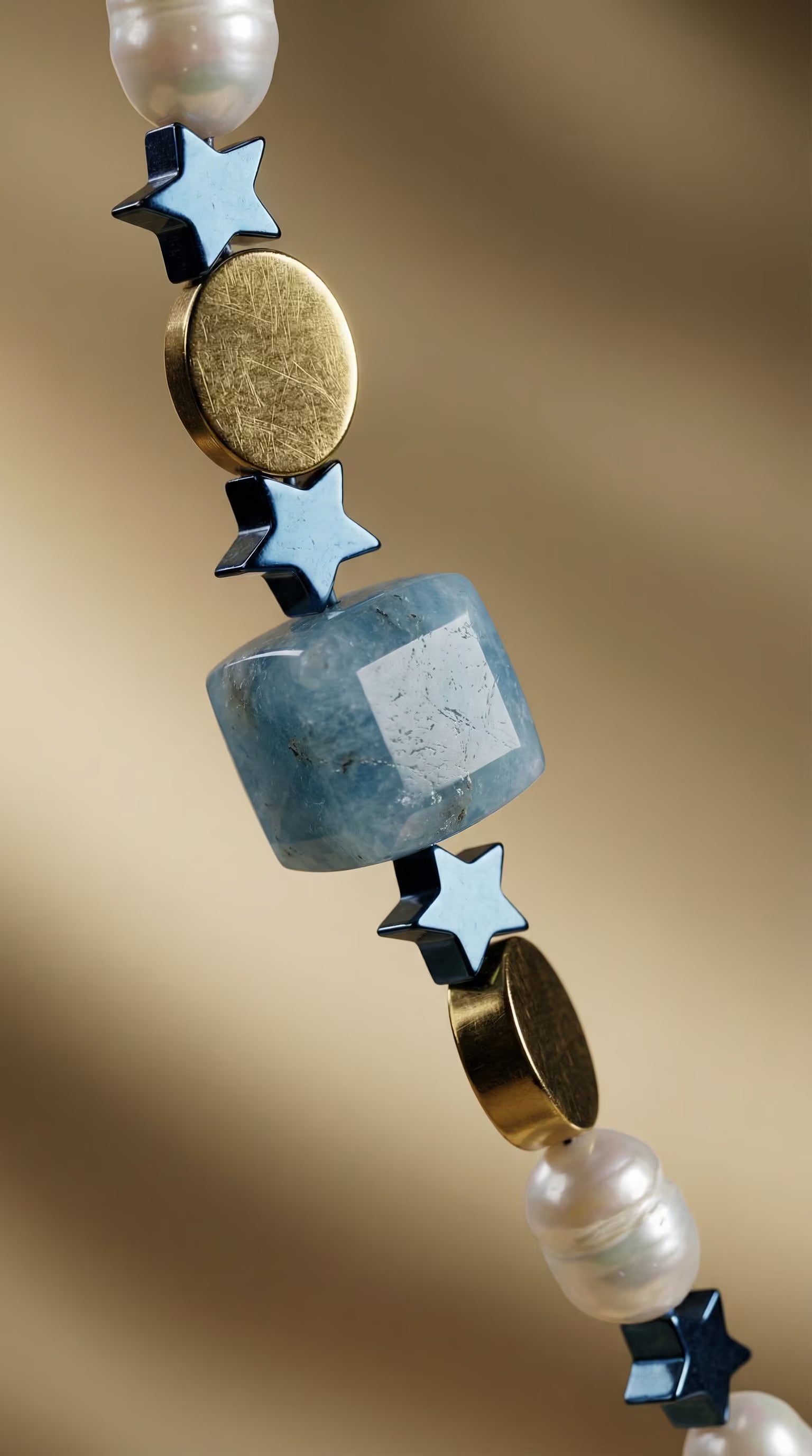 Prim-plan macro evidențiind secvența de mărgele cubice bleu stele metalice albastre discuri aurii și perle naturale inelate.