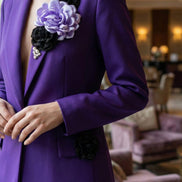 Vedere laterală a sacoului mov arătând mâneca lungă și detaliul decorativ cu floare neagră aplicată pe clapa buzunarului.