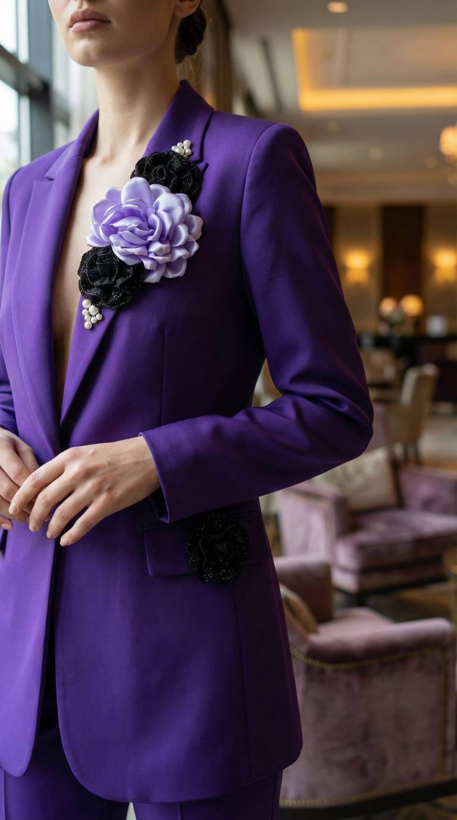 Vedere laterală a sacoului mov arătând mâneca lungă și detaliul decorativ cu floare neagră aplicată pe clapa buzunarului.