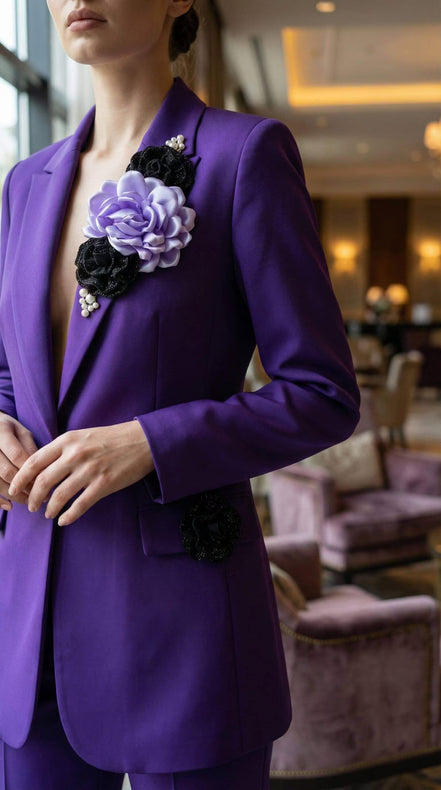 Vedere laterală a sacoului mov arătând mâneca lungă și detaliul decorativ cu floare neagră aplicată pe clapa buzunarului.