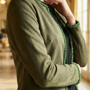 Femeie purtând o jachetă verde din material tip velur cu croială deschisă și bordură de mărgele verzi pe margini și guler.