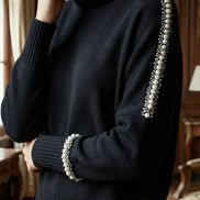 Vedere laterală a unui pulover negru tricotat cu guler rulat și decorațiuni liniare din perle pe lungimea brațului și la terminația manșetei.