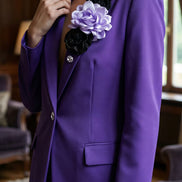 Femeie purtând un sacou mov structurat decorat pe rever cu un trandafir satinat lila și flori negre asortat cu nasture bijuterie.