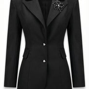 Sacou negru cambrat pozat pe manechin invizibil cu revere ascuțite satinate nasturi triunghiulari și broșă florală aplicată.