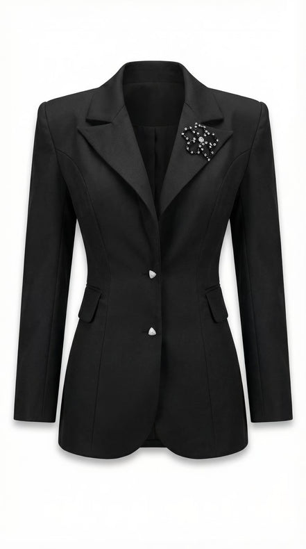 Sacou negru cambrat pozat pe manechin invizibil cu revere ascuțite satinate nasturi triunghiulari și broșă florală aplicată.