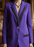 Vedere frontală a unui sacou mov purtat de model evidențiind croiala dreaptă și detaliile strălucitoare de pe reverele negre.