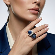 Femeie purtând un sacou albastru și un inel masiv cu pietre naturale asortat cromatic într-un cadru luminos.