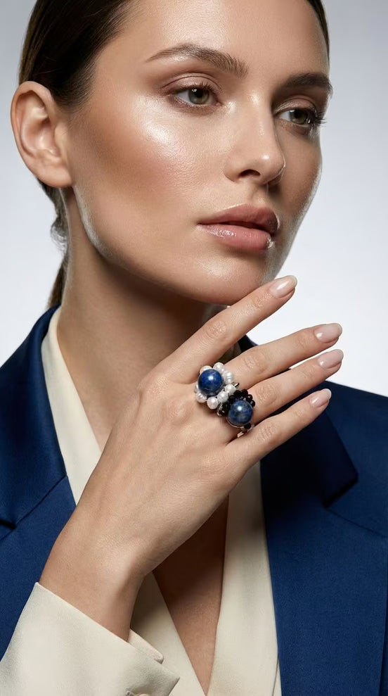 Femeie purtând un sacou albastru și un inel masiv cu pietre naturale asortat cromatic într-un cadru luminos.