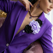 Model într-o ținută elegantă purtând sacou mov cu decorațiuni florale asortat cu cercei și colier din pietre mov într-un decor clasic.